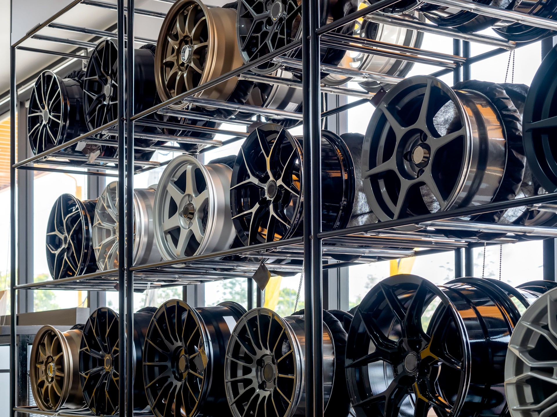 Scene of modern tyre store decoration with various designs of steel alloy wheels rim on metal shelf inside the building near huge glass window. Alloy wheel showroom shop background.